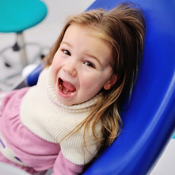A little girl sitting in the dentist’s chair with her mouth open in preparation for fluoride treatments