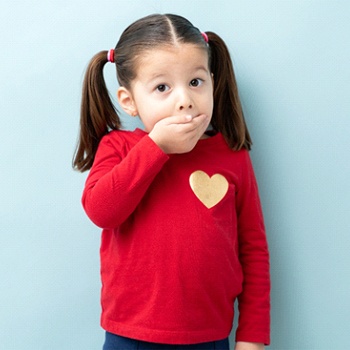A little girl with pigtails covering her mouth with her hand