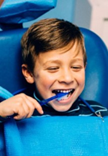 Young boy smiling while brushing his teeth at dentist's office